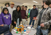 Several students standing around a gingerbread house that says "Econ" on it
