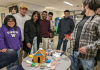 Several students standing around a gingerbread house that says "Econ" on it